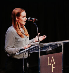 Lauren Delbridge presents at a podium emblazoned with the LAF logo