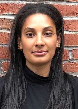 Celina Abba smiles in front of a brick wall.