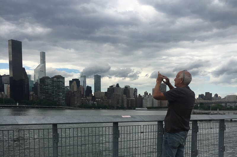 An image of a man taking a picture of the Manhattan skyline from Hunter's Point South Park