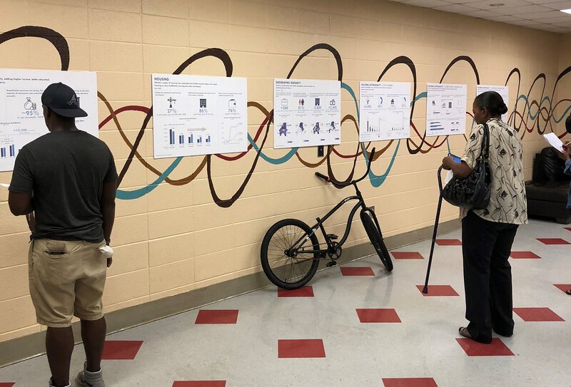 Two people view posters in a hallway. The posters have graphs and pictures on them.