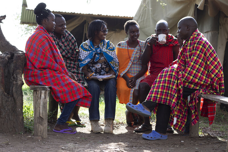 2019 CSI research assistant Carolyne Wanza Nthiwa sits and talks with Maasai community members on wooden benches