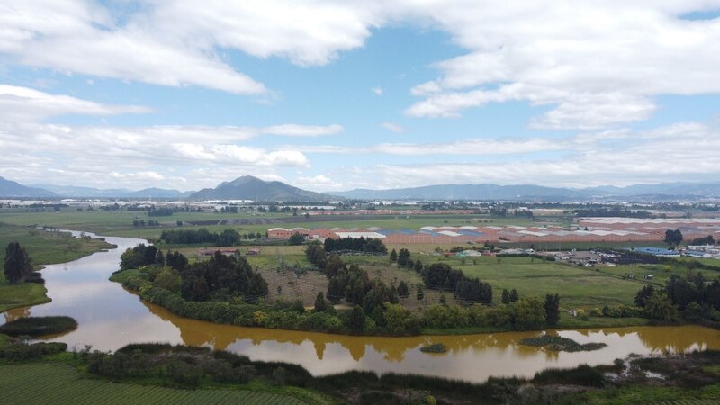 A brown-colored rivers flows through agricultural land in Colombia