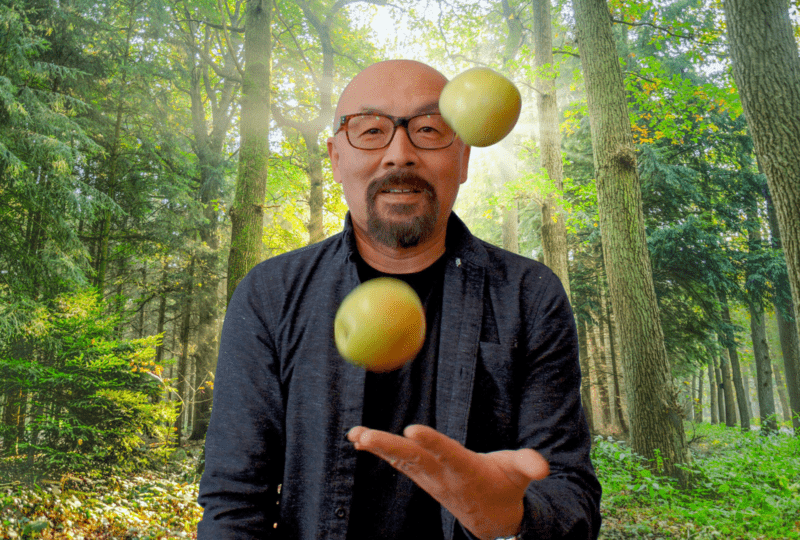 Jeff Lee juggling apples in front of a forest backdrop