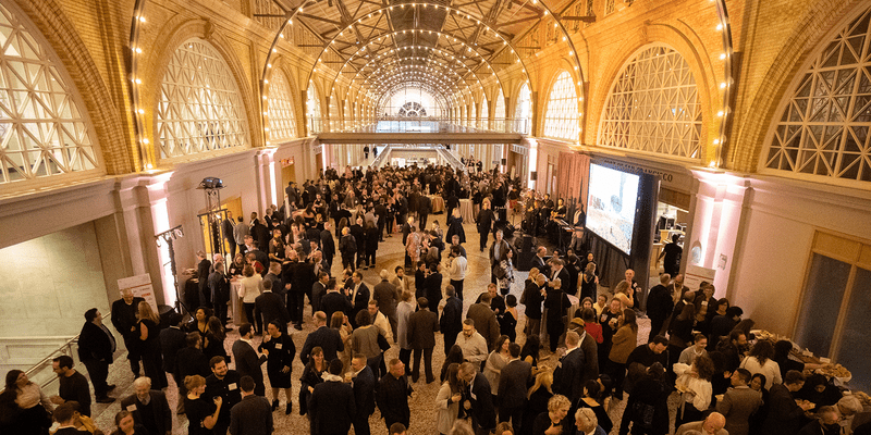 A large crowd of guests mingle under the lighted arches of the San Francisco Ferry Building's Grand Hall