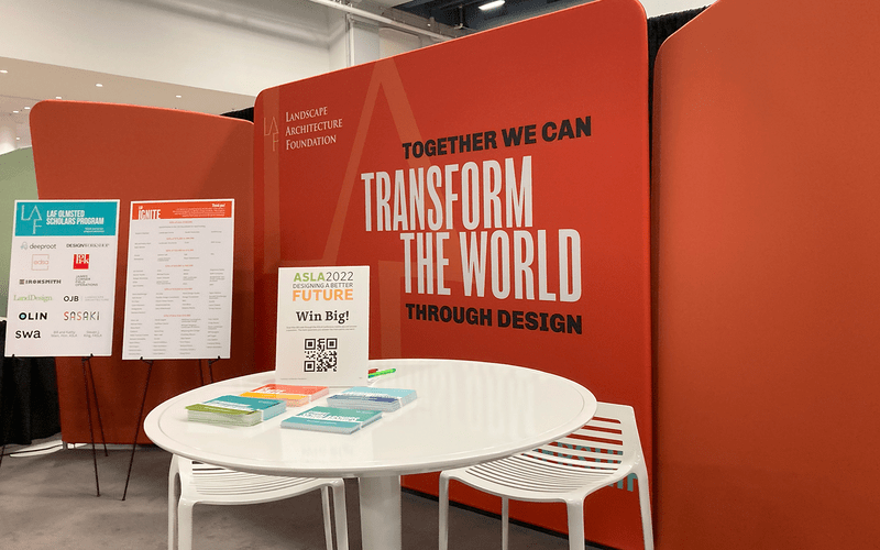 LAF EXPO booth with a white table and postcards in front of a coral red backdrop 