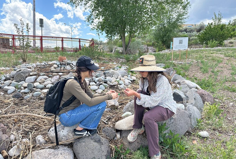 Two women sit on rocks and collect a soil core sample