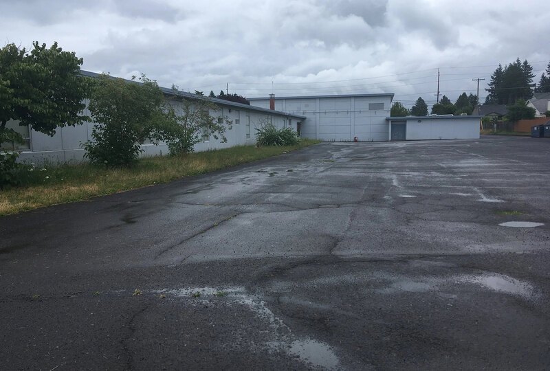 A large, empty asphalt area next to a school building with small puddles and visible cracks in the pavement