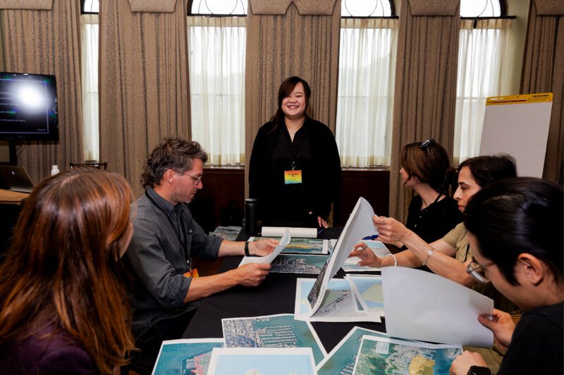 image of a woman at the head of a table with others seated and reading paper materials