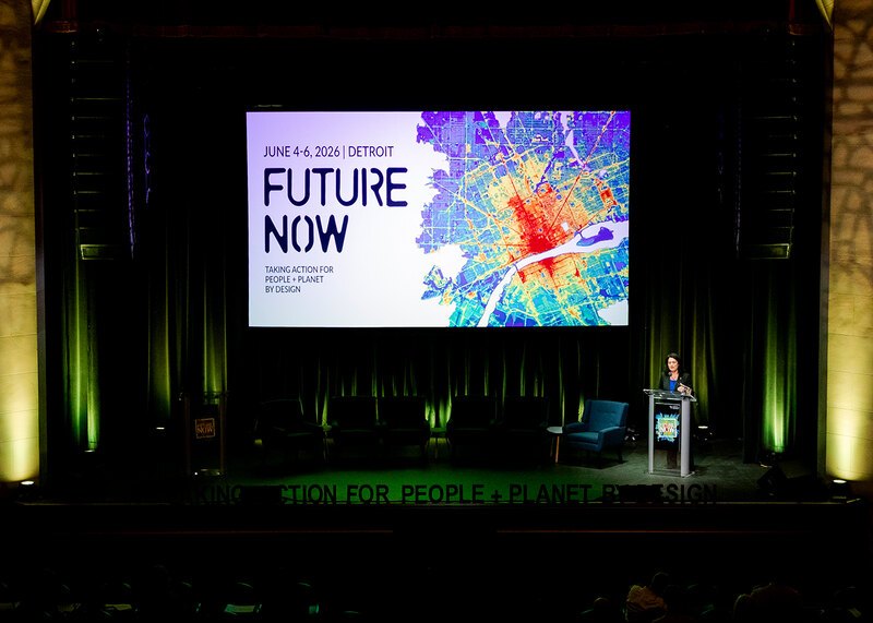 Barbara Deutsch stands at a podium on a stage with a large screen that says "Future Now" in the background