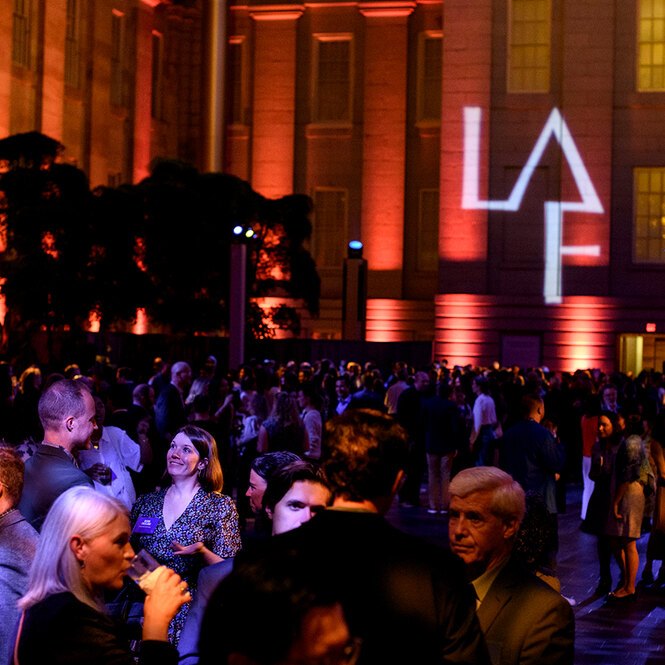 With a projection of the LAF logo on the wall in the background, attendees at LAF's 2024 Annual Benefit cluster in small groups.