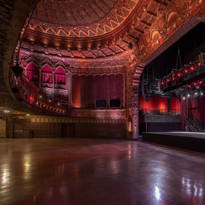 Ornate historic theater interior with gilded details, red lighting, and a stage set for an event