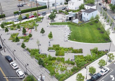 Looking down on a plaza with patterned gray brick, a lawn area, and rain gardens