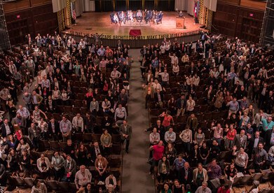A theater of people facing up toward the photographer on the balcony