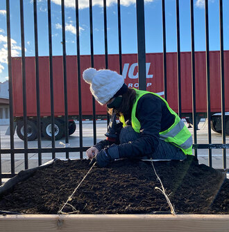 A researcher ties twine across a raised bed of soil adjacent to a highway with a semi truck in the background