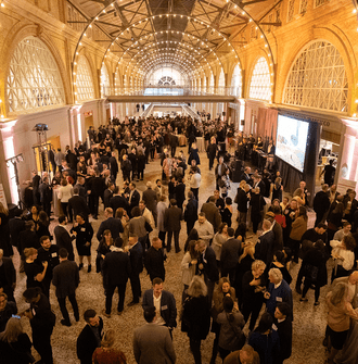 A large crowd of guests mingle under the lighted arches of the San Francisco Ferry Building's Grand Hall