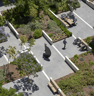 A view looking down on a designed courtyard with planted areas, sculpture, and seating