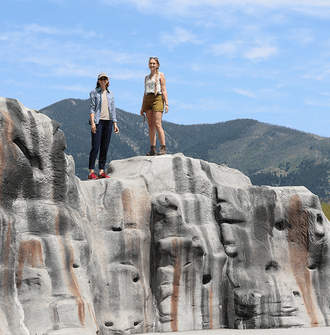 Two researchers stand atop a rock-like play structure with a mountain in the background