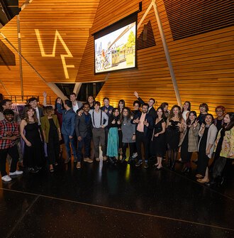 The 2023 Olmsted Scholars pose beneath the LAF logo project on a wood panel ceiling.