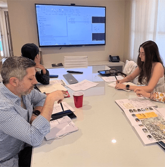 Three people sit around a conference room table looking at plans and writing in notebooks