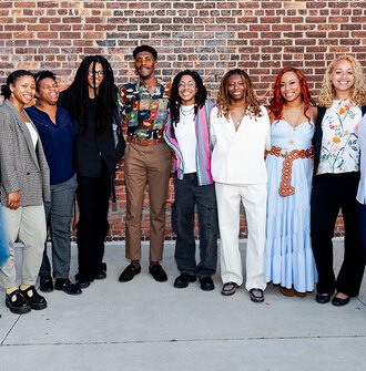 A group of eight Ignite students smiling in front of a brick wall