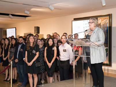 Stephanie Rolley, President of LAF, makes her closing remarks from a podium at the LAF Annual Benefit while a large group of student leaders looks on