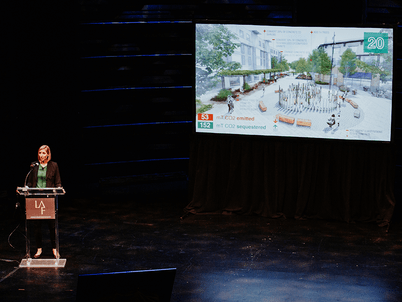 Pamela at a podium presenting with a slide of a rendering of a landscape project with quantified carbon emissions and sequestration