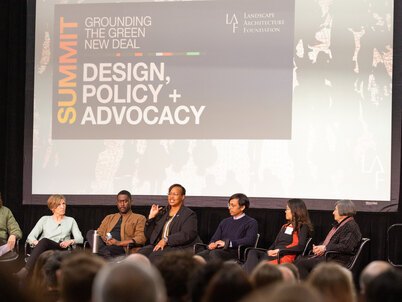 An image of seven people seated on a stage with a background screen labeled "Grounding the Green New Deal Summit: Design, Policy + Advocacy"