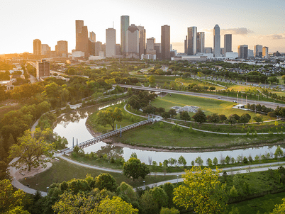 Trails and channels of water run through Buffalo Bayou Park, with the Houston skyline in the background