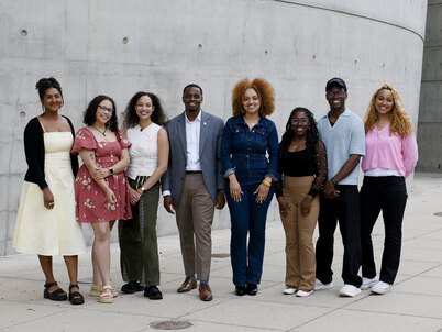 A group of 8 LAF Ignite students stand in front of a curved concrete wall.