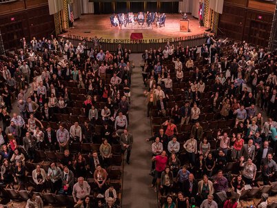 A theater of people facing up toward the photographer on the balcony