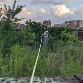 A student Research Assistant with a measuring tape in an urban patch of vegetation