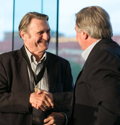 Photo of Grant Jones wearing the LAF medal, smiling, and shaking the hand of a man who has his back turned to the camera