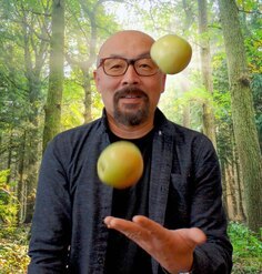 Jeff Lee juggling apples in front of a forest backdrop