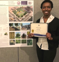 Ayana Belk holding a certificate award in front of a poster for her Reviving Troost work