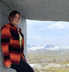 Kathryn Finnigan standing against a granite wall against a backdrop of mountainous landscape