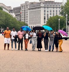 10 LAF Ignite students pose smiling on a busy pedestrian street with some holding umbrellas
